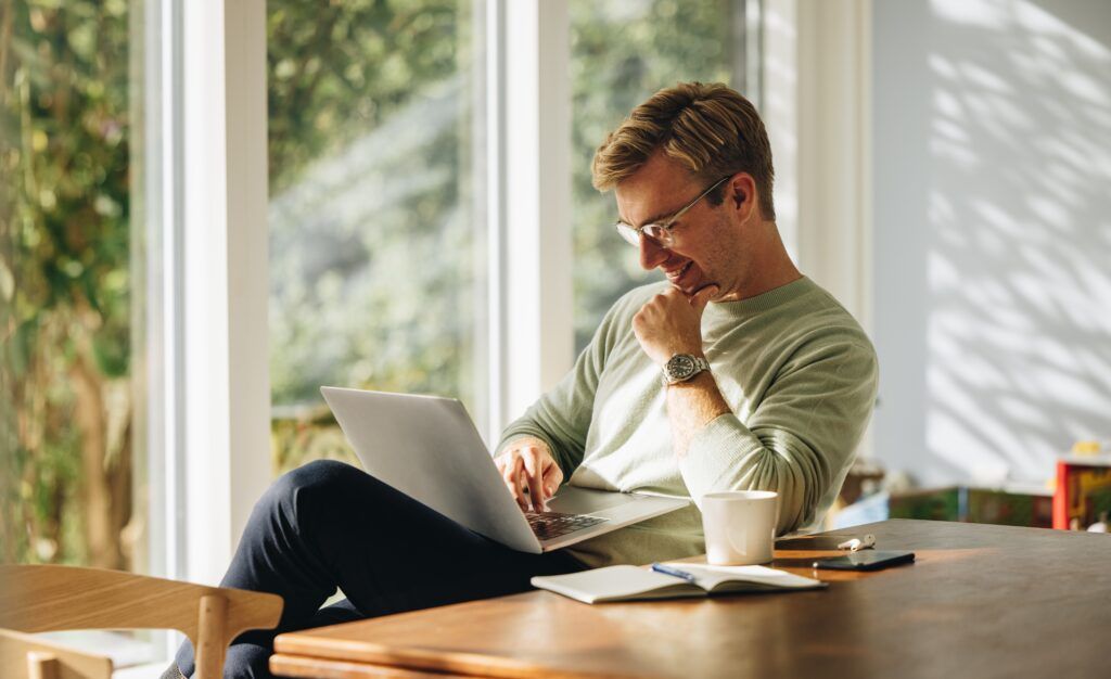 Man sitting by table working on laptop computer.