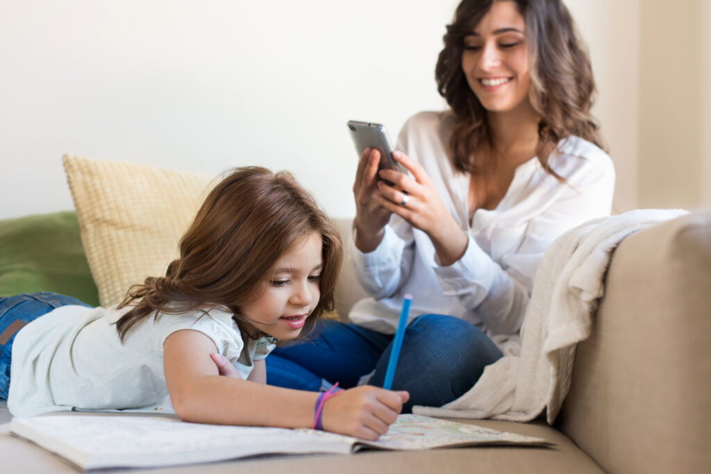 Little girl painting in the living room while mom is on phone