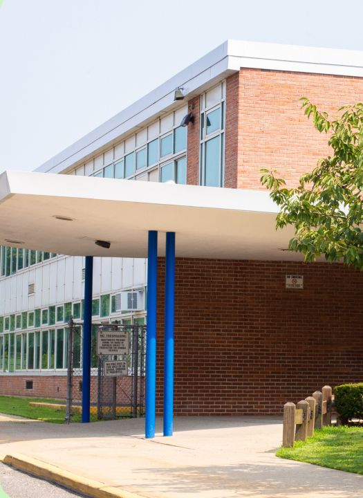 Exterior of a brick school building with a white covered walkway supported by blue pillars.
