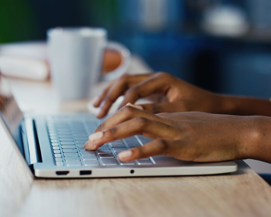 A close-up, side-angle shot of a person’s hands typing on a silver laptop keyboard.
