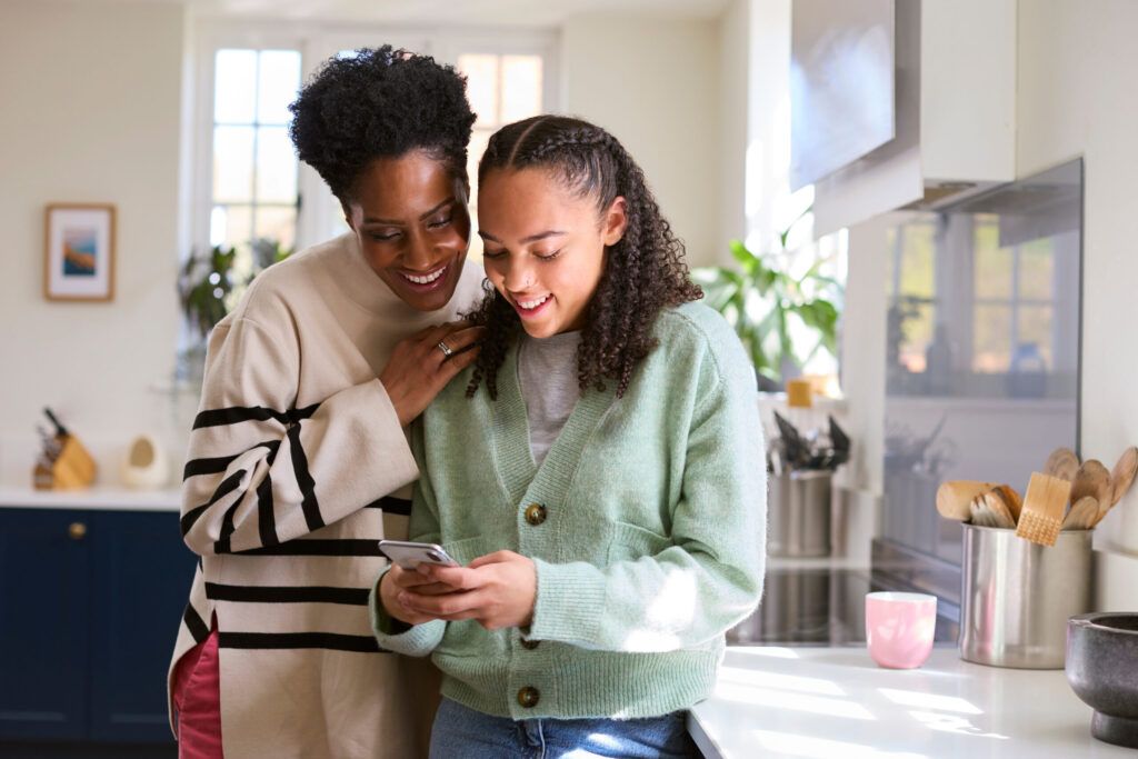 mother talking with teenage daughter at home and looking at mobile phone together