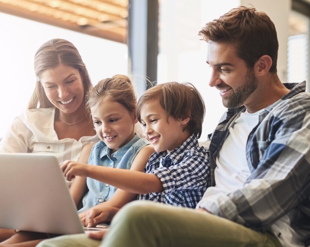 mother and father using a laptop with their son and daughter on the sofa at home.