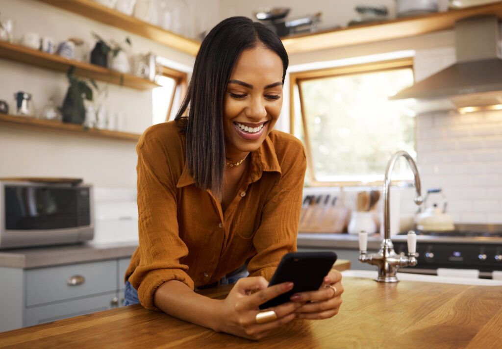Happy woman reading from phone in kitchen